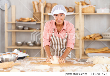 Elderly female baker kneading dough on table Elderly female baker kneading dough on table 119281475