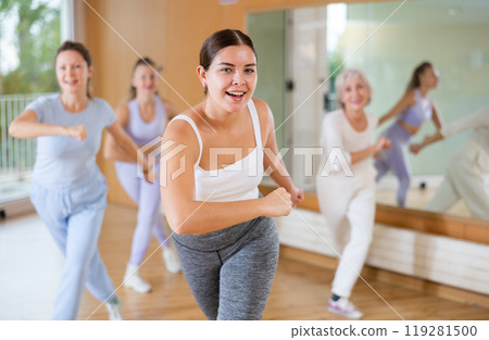 Group of happy young mature sports women in activewear exercising dynamic dancing movemens in modern gym studio Group of happy young mature sports women in activewear exercising dynamic dancing movemens in modern gym studio 119281500