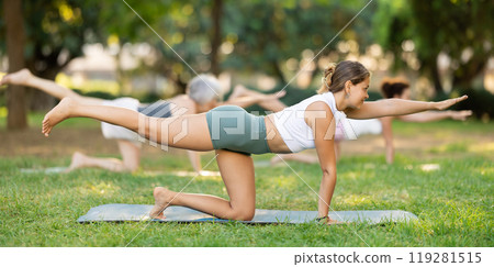 Girl performing balancing table asana during group yoga in park 119281515
