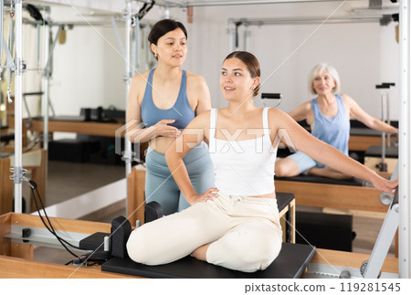 Girl doing pilates exercises on reformer with asian female instructor 119281545