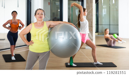 Portrait of mature woman standing with fitness ball during group training at gym 119281551