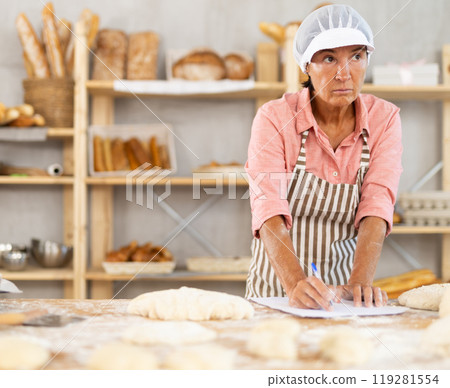 Mature baker woman rolling dough with a pin in a bakery 119281554