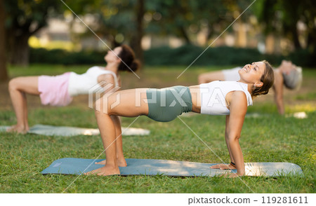 Girl performing Reverse Table Pose during group yoga outdoors 119281611