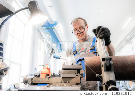 A technician operates a lathe machine in an industrial workspace, meticulously adjusting a metal A technician operates a lathe machine in an industrial workspace, meticulously adjusting a metal 119281913