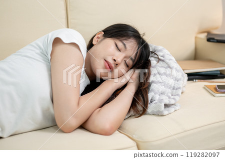 A pretty, happy young Asian woman in comfy clothes is taking a nap on a sofa in the living room. A pretty, happy young Asian woman in comfy clothes is taking a nap on a sofa in the living room. 119282097