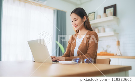 Beautiful young Asian woman working with laptop computer in home kitchen Beautiful young Asian woman working with laptop computer in home kitchen 119283665