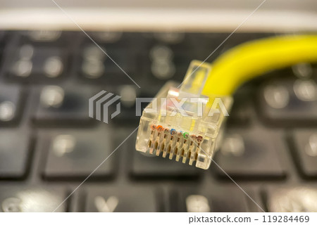 Ethernet Cable Close-up.A close-up photo of an Ethernet cable connector, showcasing the eight colored wires inside. The cable is yellow and is positioned above a laptop keyboard. 119284469