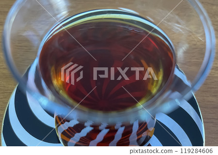 A close-up photo of a glass of dark tea, possibly Turkish tea, resting on a saucer with a swirling black and white pattern. A close-up photo of a glass of dark tea, possibly Turkish tea, resting on a saucer with a swirling black and white pattern. 119284606