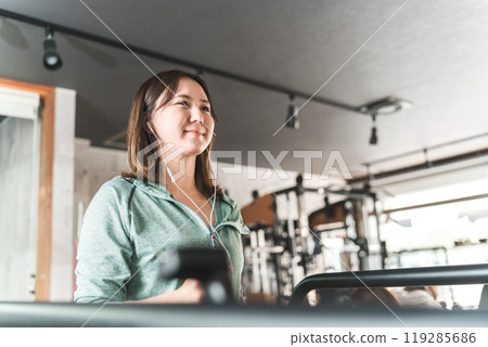 Asian woman walking and doing aerobic exercise on a treadmill/running machine in a sports gym 119285686