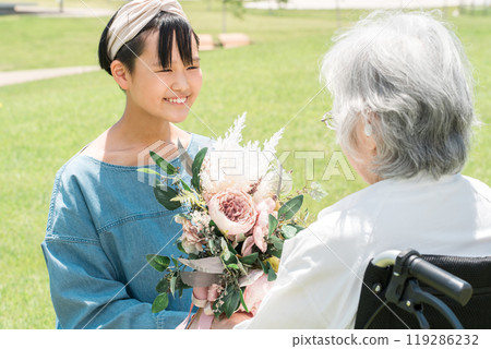 Smiling granddaughter presents a bouquet of flowers to her grandmother in a wheelchair 119286232