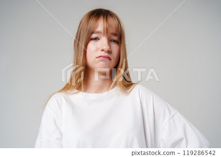 A young girl with long hair looks unimpressed against a plain background A young girl with long hair looks unimpressed against a plain background 119286542