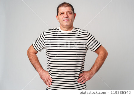 A man stands confidently in a striped shirt, casual jeans with a neutral background 119286543
