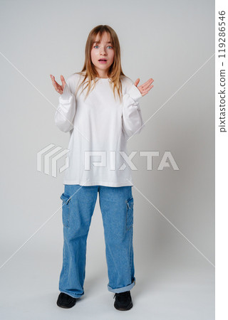 A surprised child wearing a white long-sleeve shirt and blue jeans expresses confusion in a studio setting A surprised child wearing a white long-sleeve shirt and blue jeans expresses confusion in a studio setting 119286546