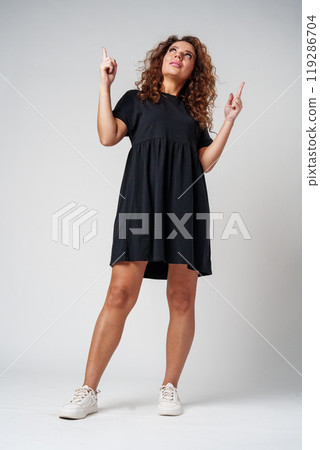 Cheerful young woman with curly hair giving a thumbs up while smiling against a neutral background Cheerful young woman with curly hair giving a thumbs up while smiling against a neutral background 119286704