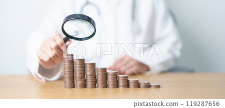Doctor with Coins money stack growing with magnifier glass. Money saving, Job search, hiring and research development, Health Insurance, Medical, Donation and Healthcare cost concepts 119287656