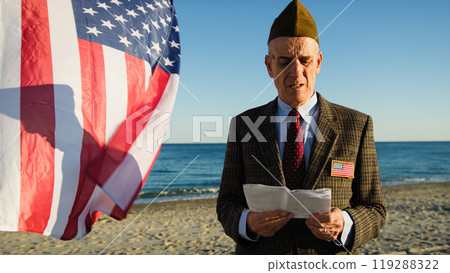 American Veteran Reads Speech On Beach In Front Of Flag Near Ocean 119288322