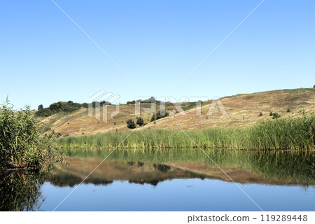 Beautiful serene river Bityug reflecting lush greenery under clear blue sky at midday Beautiful serene river Bityug reflecting lush greenery under clear blue sky at midday 119289448