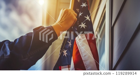 Hand raising an American flag outside a house, symbolizing patriotism, national pride, and respect for the United States 119289914
