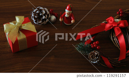 Gold and red gift boxes, Christmas wreath and Santa doll on oak wood background 119291157
