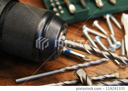 Close-up of a drill, set with drills and various materials on a wooden background. 119291335