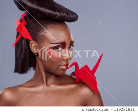 Portrait, cosmetics and black woman with origami for beauty in studio isolated on gray background. Face, creative makeup and confident serious model with red paper crane in hair, skincare and art Portrait, cosmetics and black woman with origami for beauty in studio isolated on gray background. Face, creative makeup and confident serious model with red paper crane in hair, skincare and art 119291631