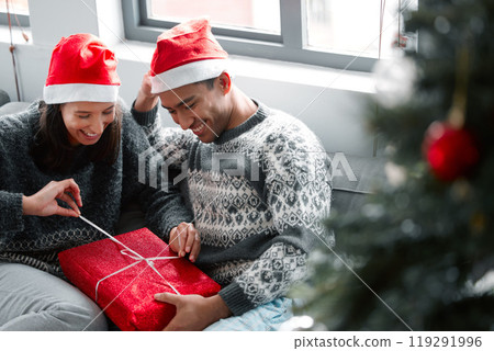 Opening, present and couple in home on Christmas with surprise in box on vacation or holiday, Excited, woman and man giving package with ribbon at event and giveaway celebration of Xmas with gift Opening, present and couple in home on Christmas with surprise in box on vacation or holiday, Excited, woman and man giving package with ribbon at event and giveaway celebration of Xmas with gift 119291996