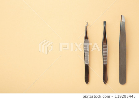 Beauty and fashion concept - tools for Eyelash Extension Procedure. Tweezers on beige background. Copyspace mockup 119293443