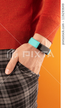 A man holding his hand with a digital bracelet in his pants pocket, bright colored background. A man holding his hand with a digital bracelet in his pants pocket, bright colored background. 119293649