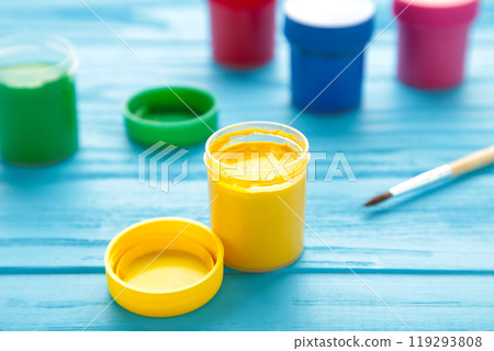 Multicolored jars of gouache and a brush on a blue background. Creative kit. 119293808