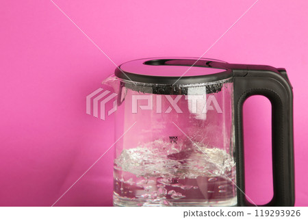 Glass electric kettle with boiling water on pink background. Glass electric kettle with boiling water on pink background. 119293926