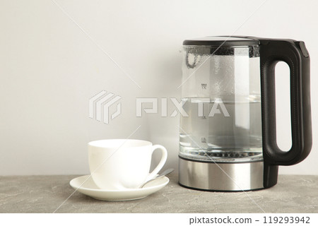 Glass electric kettle with white cup on grey background. 119293942