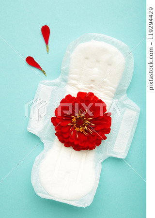White sanitary pad, hygiene protection on a blue background. Gynecological menstrual cycle. A rose flower lies on a menstrual pad. First menstruation 119294429