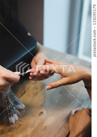 Woman getting nails done in beauty salon. Nail care procedure in a beauty salon. Female hands and tools for manicure, process of performing manicure in beauty salon.  119295179