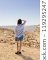 A woman is standing alone in the vast desert, curiously gazing at the distant mountains that rise majestically on the horizon 119295247