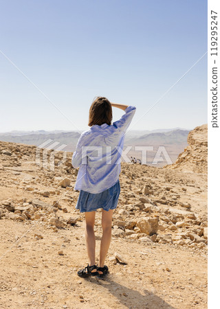 A woman is standing alone in the vast desert, curiously gazing at the distant mountains that rise majestically on the horizon 119295247