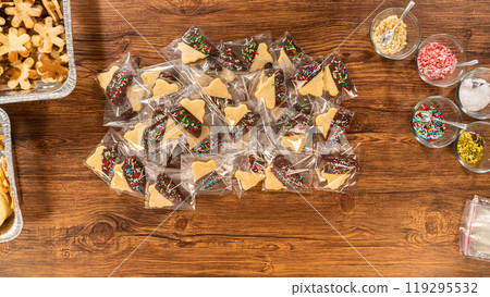 Carefully packaging Christmas cutout cookies, half-dipped in chocolate and presented in clear cellophane wrapping, perfect for festive gifting. 119295532