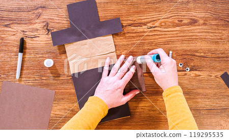 Step by step. Flat lay. Teacher guides online class through making a paper puppet from a brown bag, creatively using a wooden surface as a workspace. 119295535