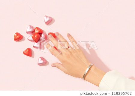 Beautiful well-groomed female hand with pink matte nails and heart-shaped candies on a pink background. Beauty salon, manicure, pedicure 119295762