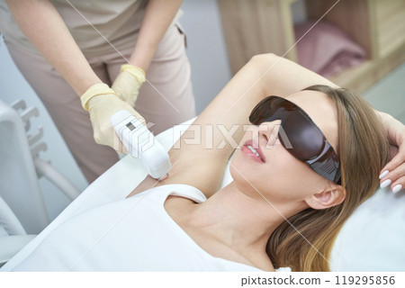 Woman receiving laser hair removal treatment on armpit in a clinic setting Woman receiving laser hair removal treatment on armpit in a clinic setting 119295856