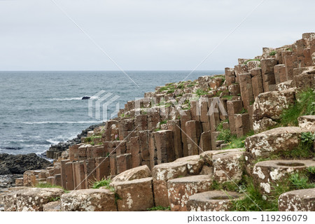 Hexagonal basalt columns of Giant Causeway slope toward the Atlantic Ocean with patches of green 119296079