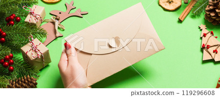Top view of woman holding an envelope on green background made of holiday decorations. Christmas time concept 119296608