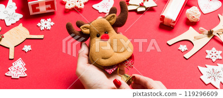 Top view of reindeer in female hands on red background. Christmas decorations. New Year holiday concept 119296609