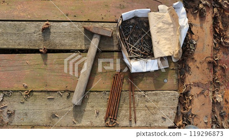 old hammer and paper box with rusty nails lying on textured worn wooden boards sprinkled with withered leaves, abandoned workplace of wood builder conceptual background 119296873