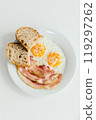 A pristine white plate beautifully topped with delicious eggs, crispy bacon, and goldenbrown bread slices that complement the meal 119297262