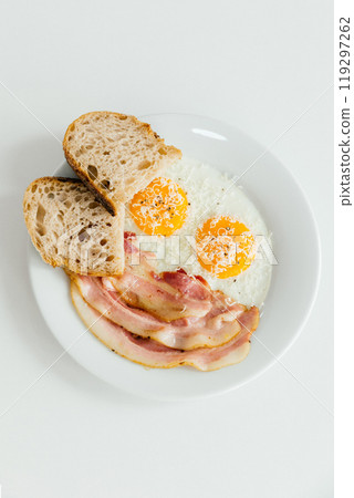 A pristine white plate beautifully topped with delicious eggs, crispy bacon, and goldenbrown bread slices that complement the meal 119297262