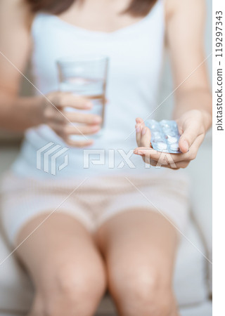 woman hand holding medicine painkiller pill and water glass on the sofa at home, taking for headaches, stomach ache, Diarrhea Pain from food poisoning, Endometriosis, Hysterectomy and Menstrual 119297343