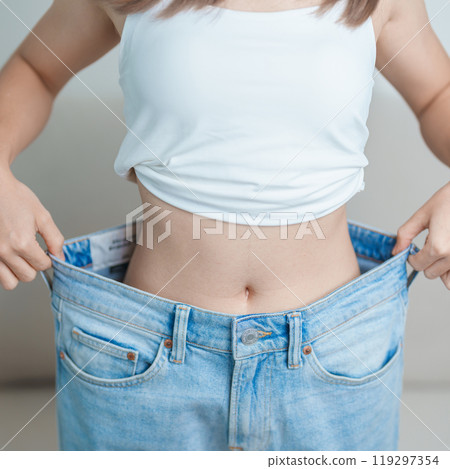 young slim female wearing big or oversize jeans, woman show healthy shape after weight loss. dieting, exercise, body fit and liposuction surgery concept young slim female wearing big or oversize jeans, woman show healthy shape after weight loss. dieting, exercise, body fit and liposuction surgery concept 119297354