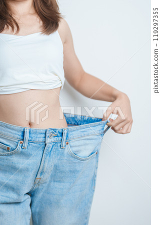 young slim female wearing big or oversize jeans, woman show healthy shape after weight loss. dieting, exercise, body fit and liposuction surgery concept young slim female wearing big or oversize jeans, woman show healthy shape after weight loss. dieting, exercise, body fit and liposuction surgery concept 119297355