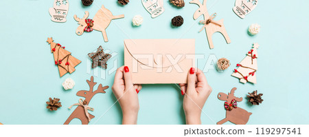 Top view of woman holding an envelope on blue background made of holiday decorations. Christmas time concept Top view of woman holding an envelope on blue background made of holiday decorations. Christmas time concept 119297541
