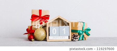 1 january. Christmas composition on colored background with a wooden calendar, with a gift box, toys, bauble copy space 1 january. Christmas composition on colored background with a wooden calendar, with a gift box, toys, bauble copy space 119297600